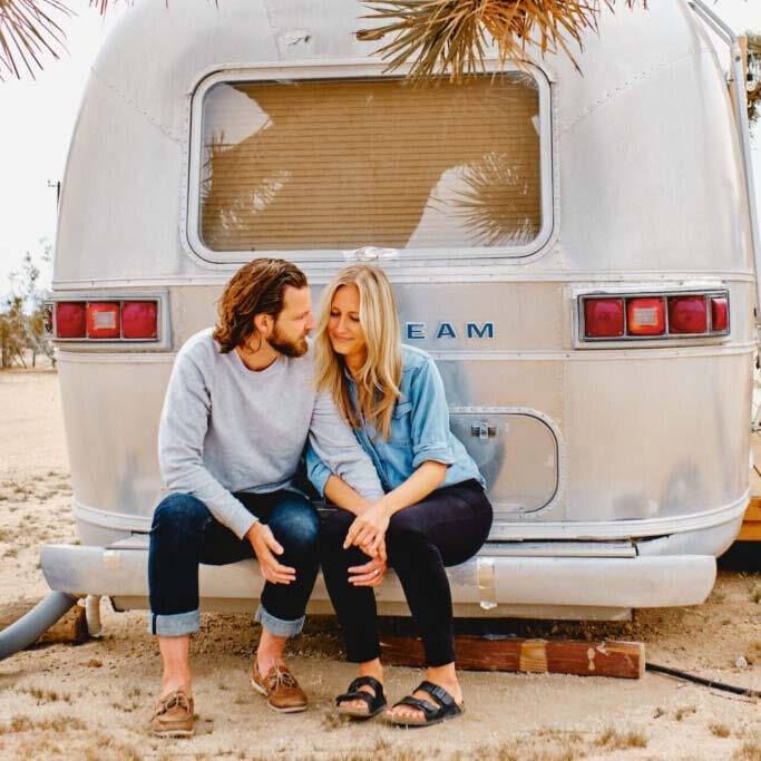 Lucy und Harry sitzen an einem silbernen Airstream-Wohnwagen in der Wüste, Kalifornien