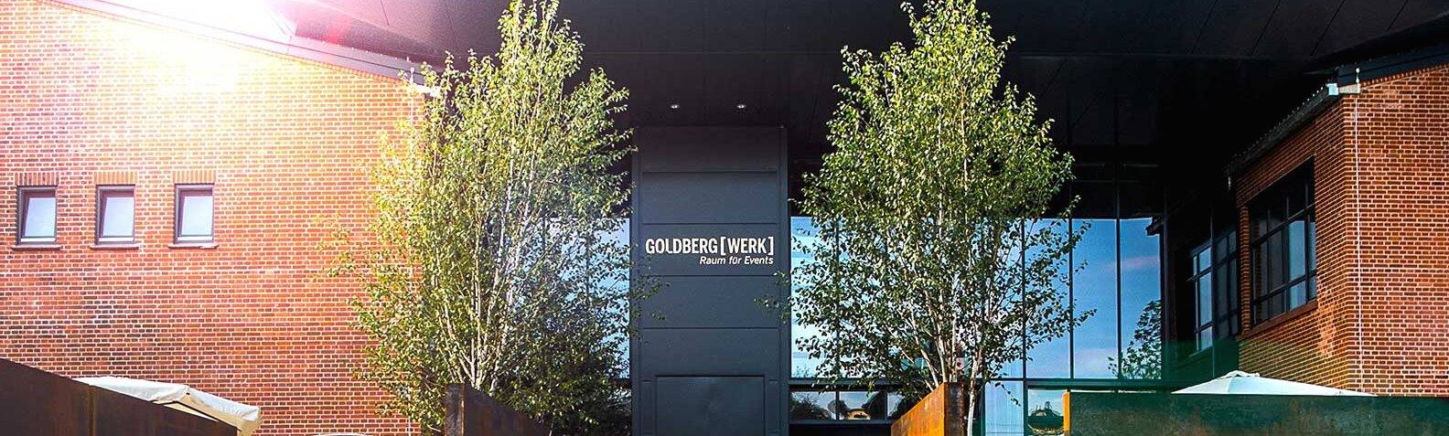 Außenansicht des Goldbergwerks Fellbach: Backsteinbau mit Schriftzug und jungen Bäumen
