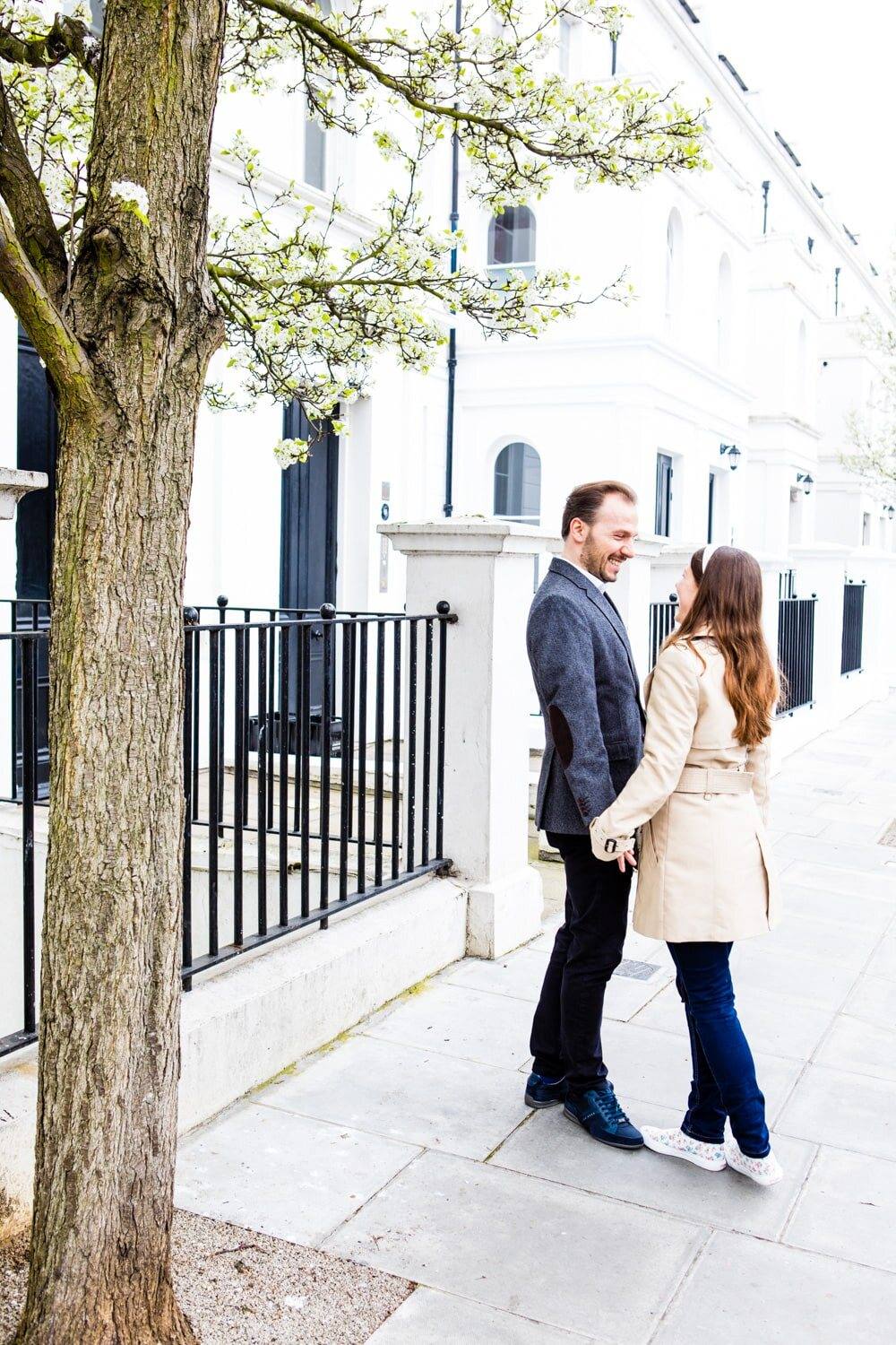 Paar auf einem Gehweg vor weißen Stadthäusern mit blühendem Baum, London