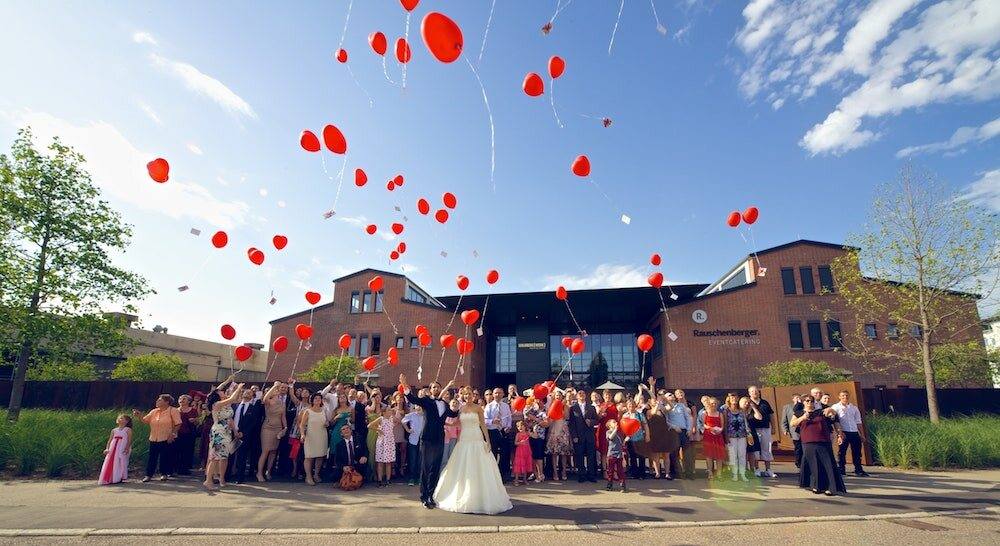 Hochzeitsgesellschaft lässt rote Herzballons vor dem Goldbergwerk Fellbach steigen