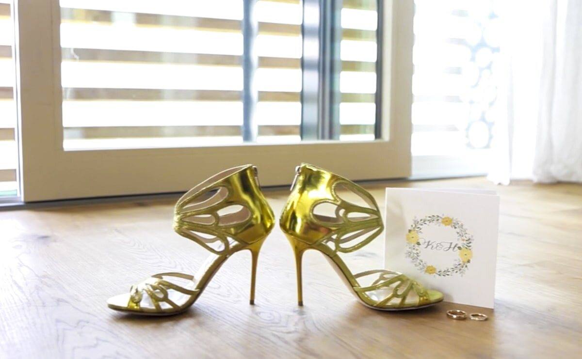 Goldene Riemchen-Heels und Karte mit Blumenkranz auf Holzboden
