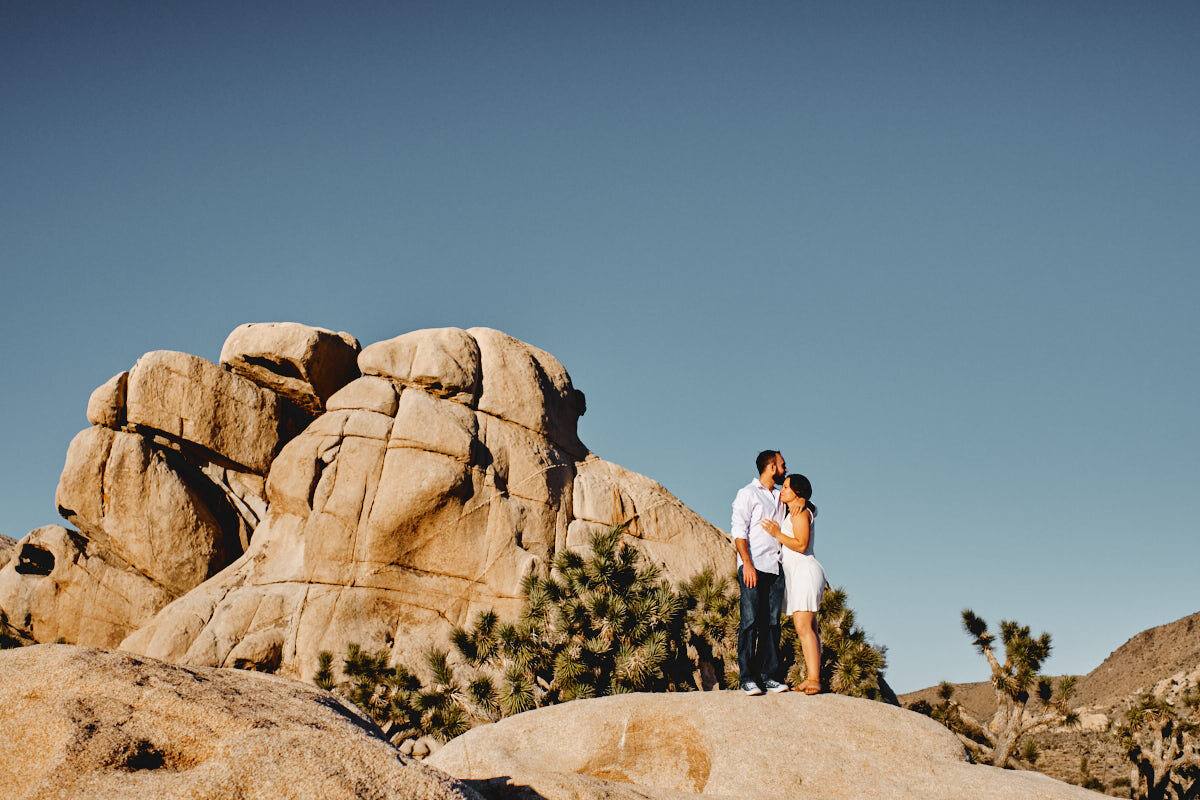 Paar auf einer Felsformation vor tiefblauem Himmel, Joshua Tree Nationalpark