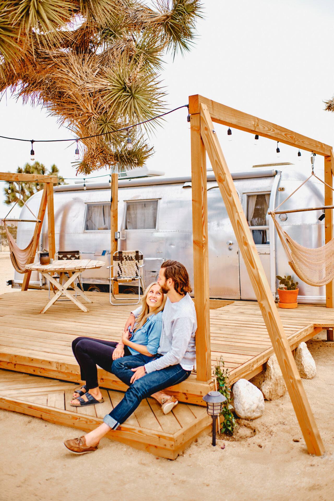 Paar auf dem Holzdeck vor dem Airstream mit Lichterkette, Joshua Tree