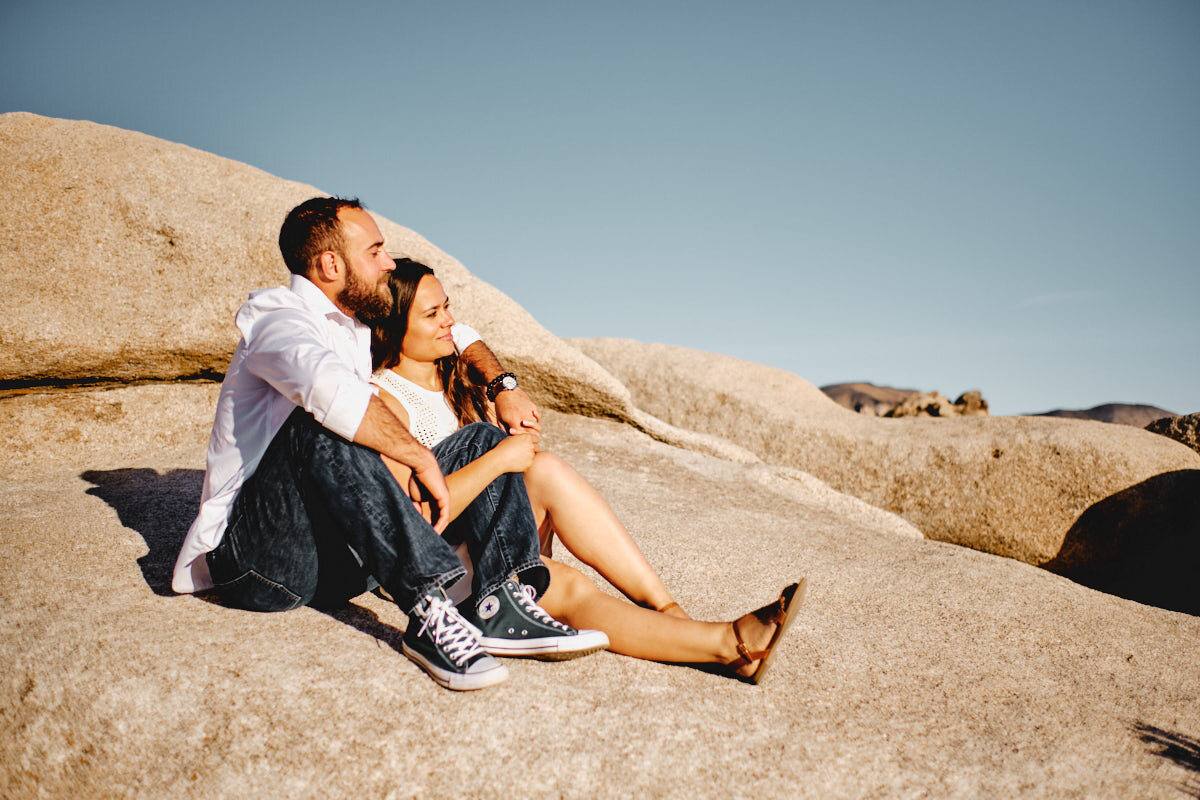 Verlobtes Paar sitzt entspannt auf einer Felsplatte im Joshua Tree Nationalpark