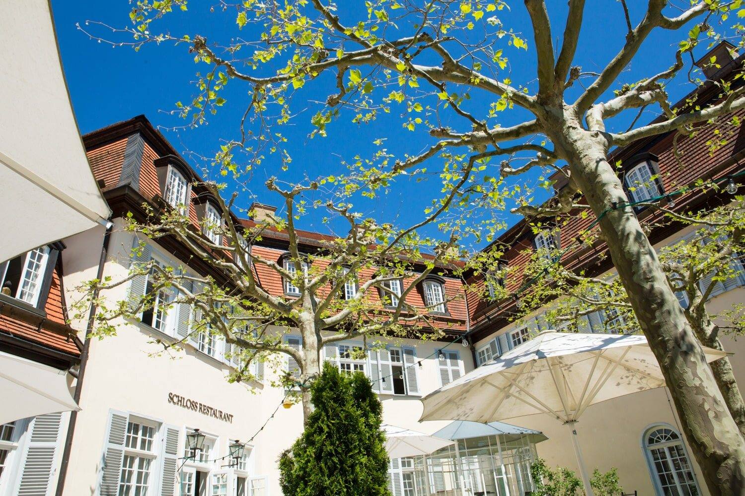 Innenhof der Schlossgastronomie mit Sonnenschirmen und Platane, Schloss Solitude