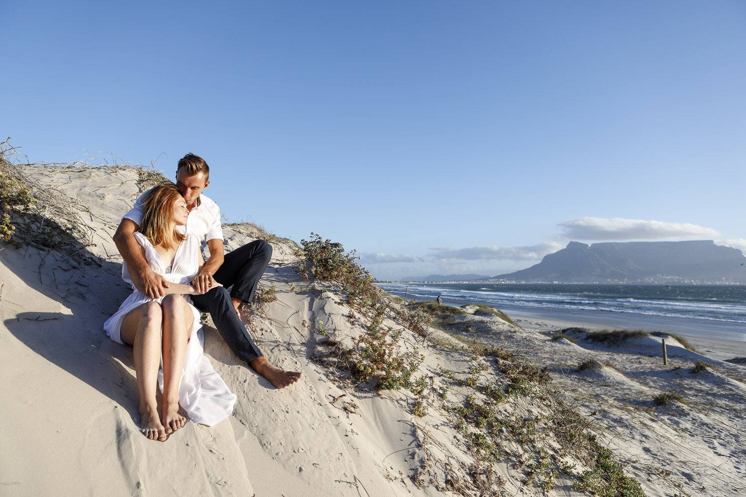 Diana und Tim sitzen in den Dünen mit Blick über die Bucht auf den Tafelberg