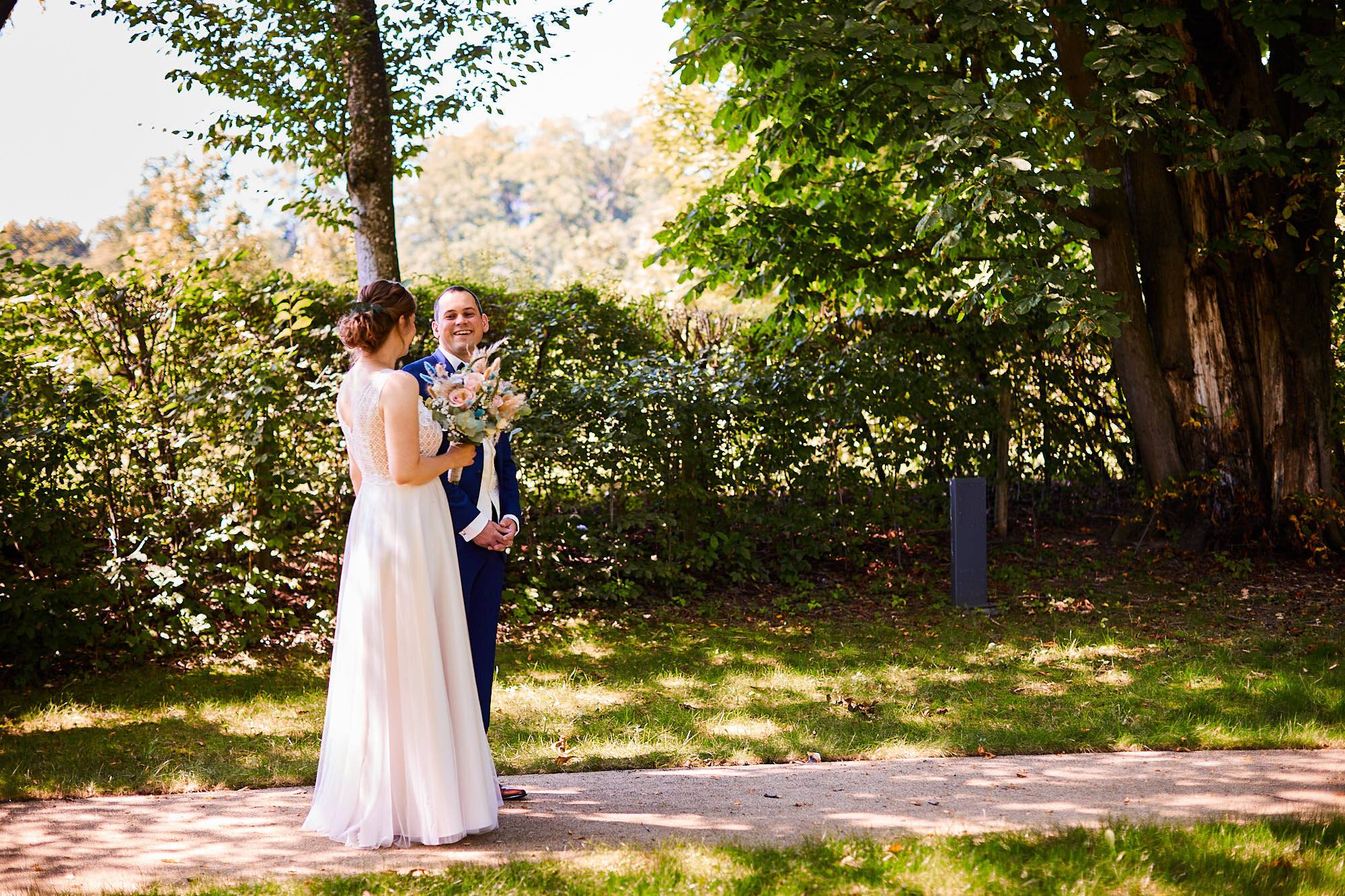 Brautpaar begegnet sich beim First Look vor einer grünen Hecke