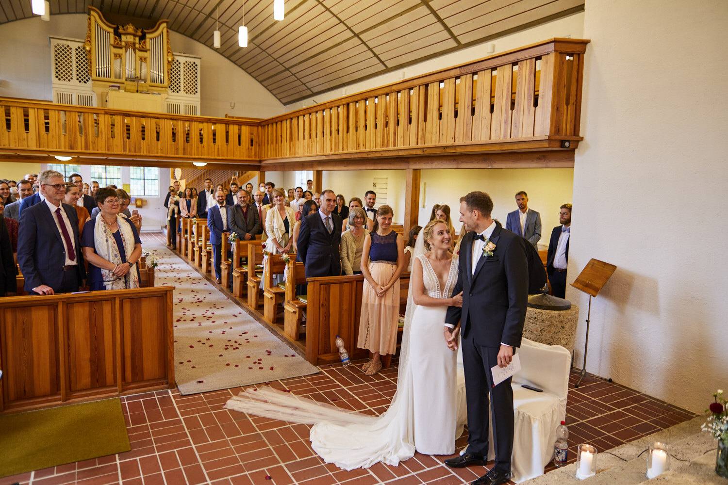 Brautpaar vor dem Pfarrer, Blick durch das Kirchenschiff mit Empore und Orgel
