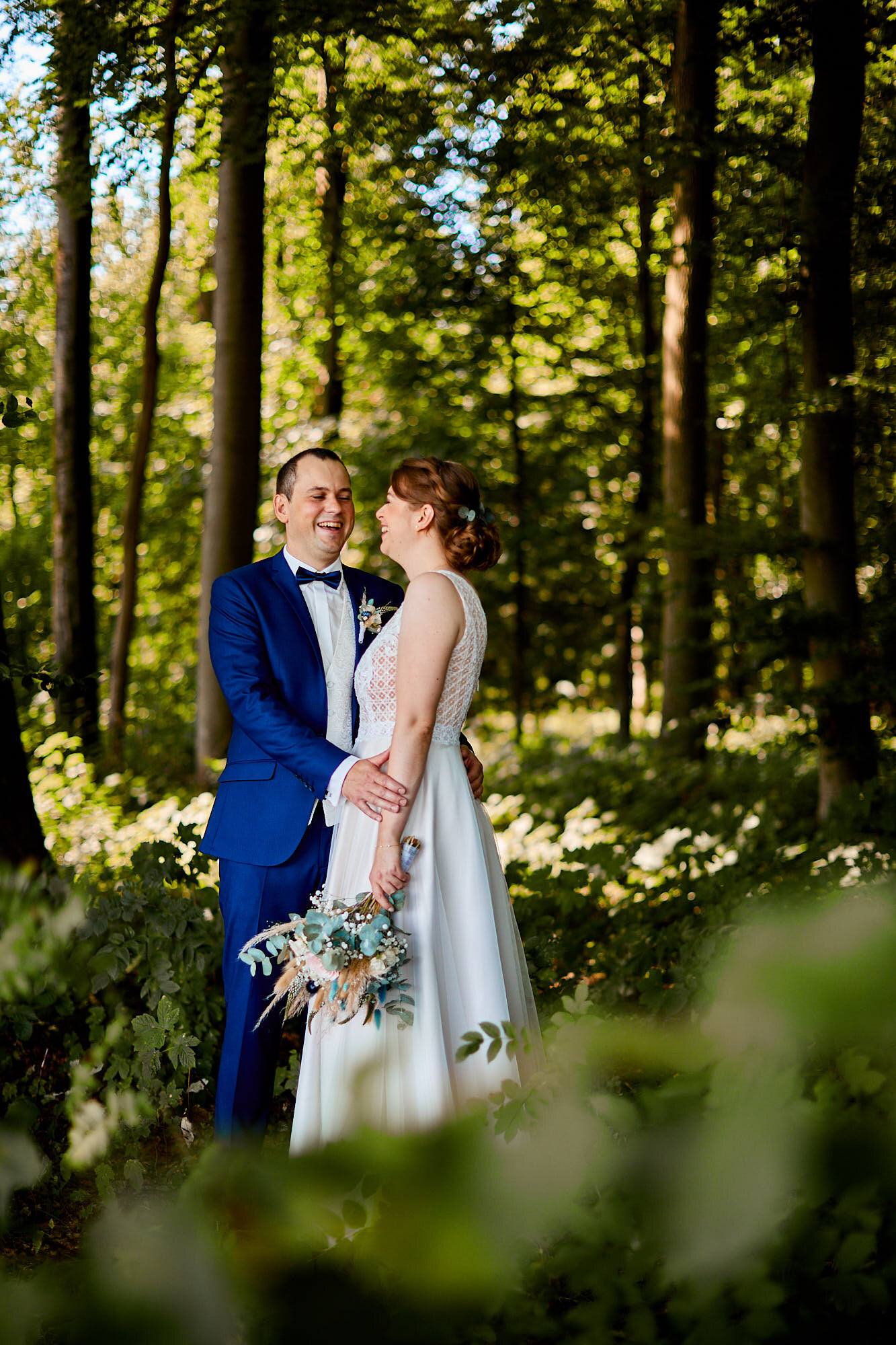 Lachendes Brautpaar in enger Umarmung im Wald.