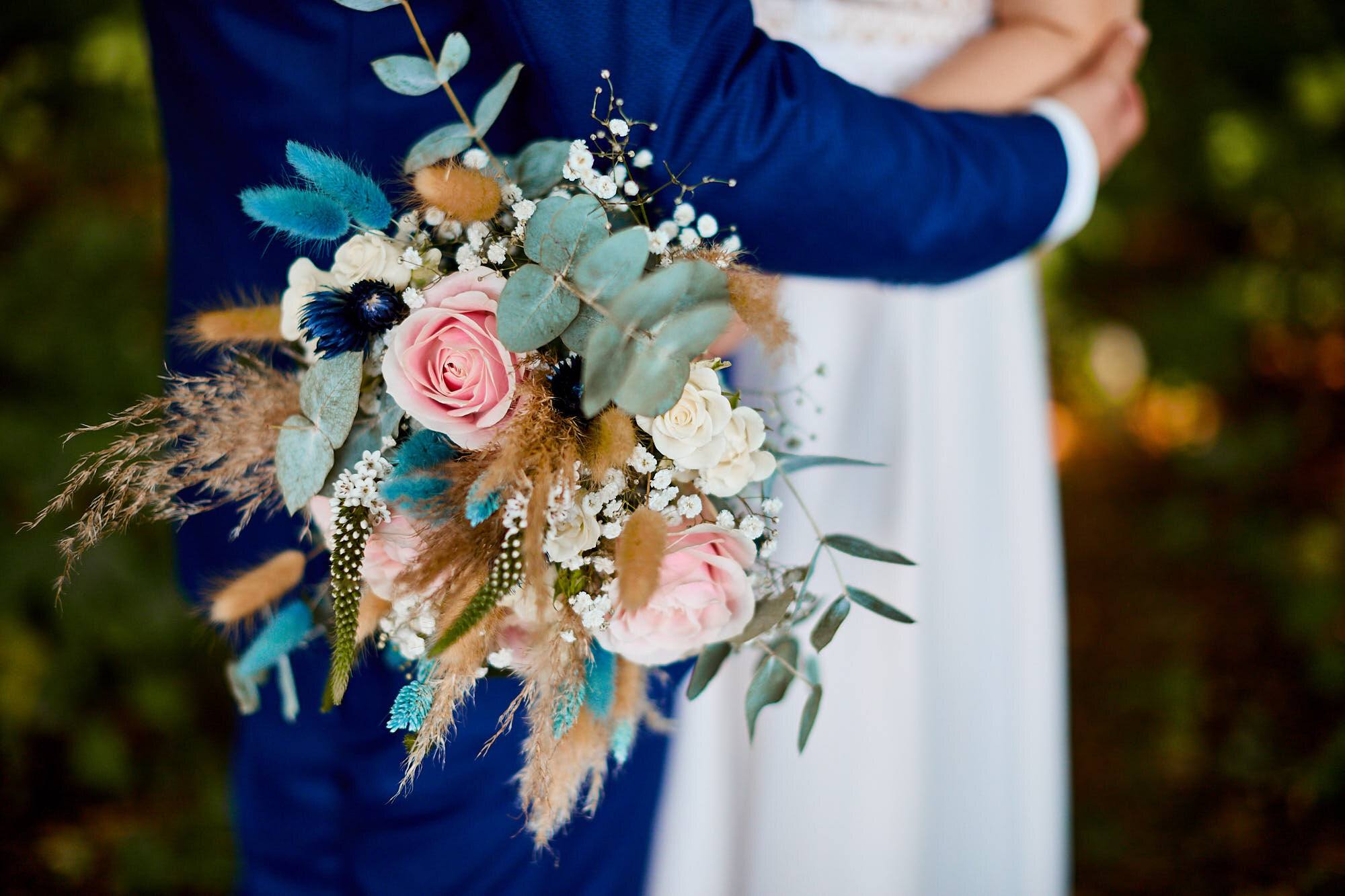 Brautstrauß mit rosa Rosen, Eukalyptus und Trockenblumen hinter dem Bräutigam