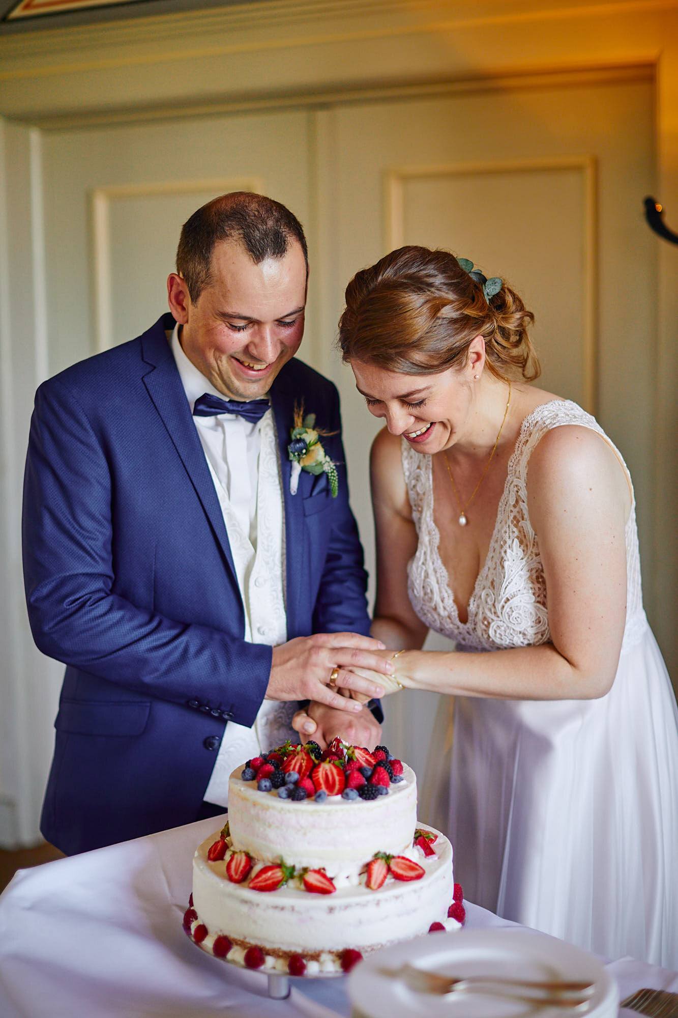 Brautpaar schneidet lachend die Hochzeitstorte mit Beeren an