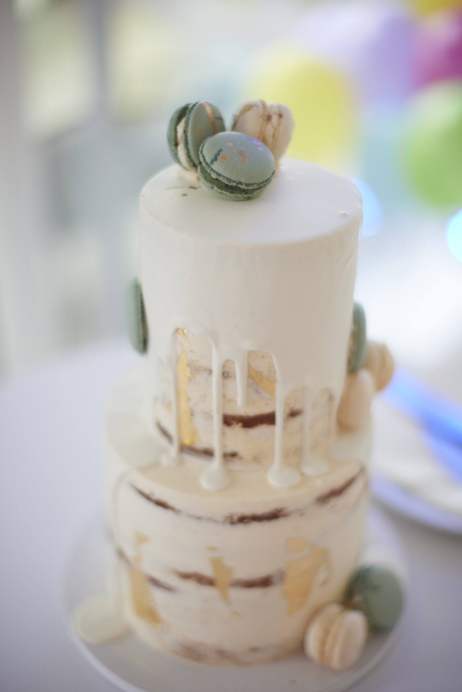 Hochzeitstorte mit Macarons und Goldflocken vor farbigem Hintergrund