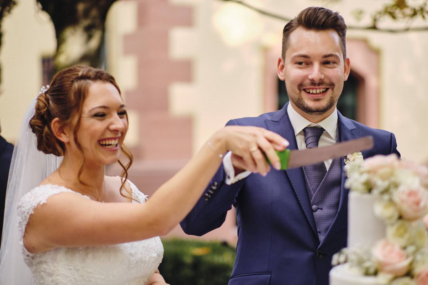 Brautpaar schneidet lachend die Hochzeitstorte an