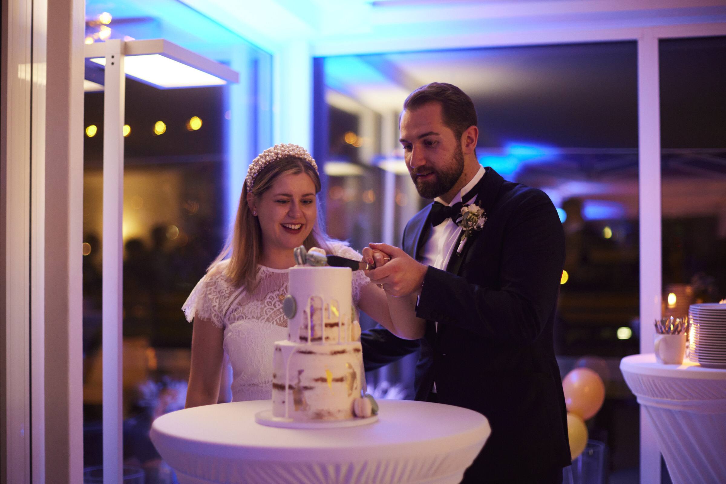 Brautpaar schneidet die Hochzeitstorte im blauen und lila Licht an
