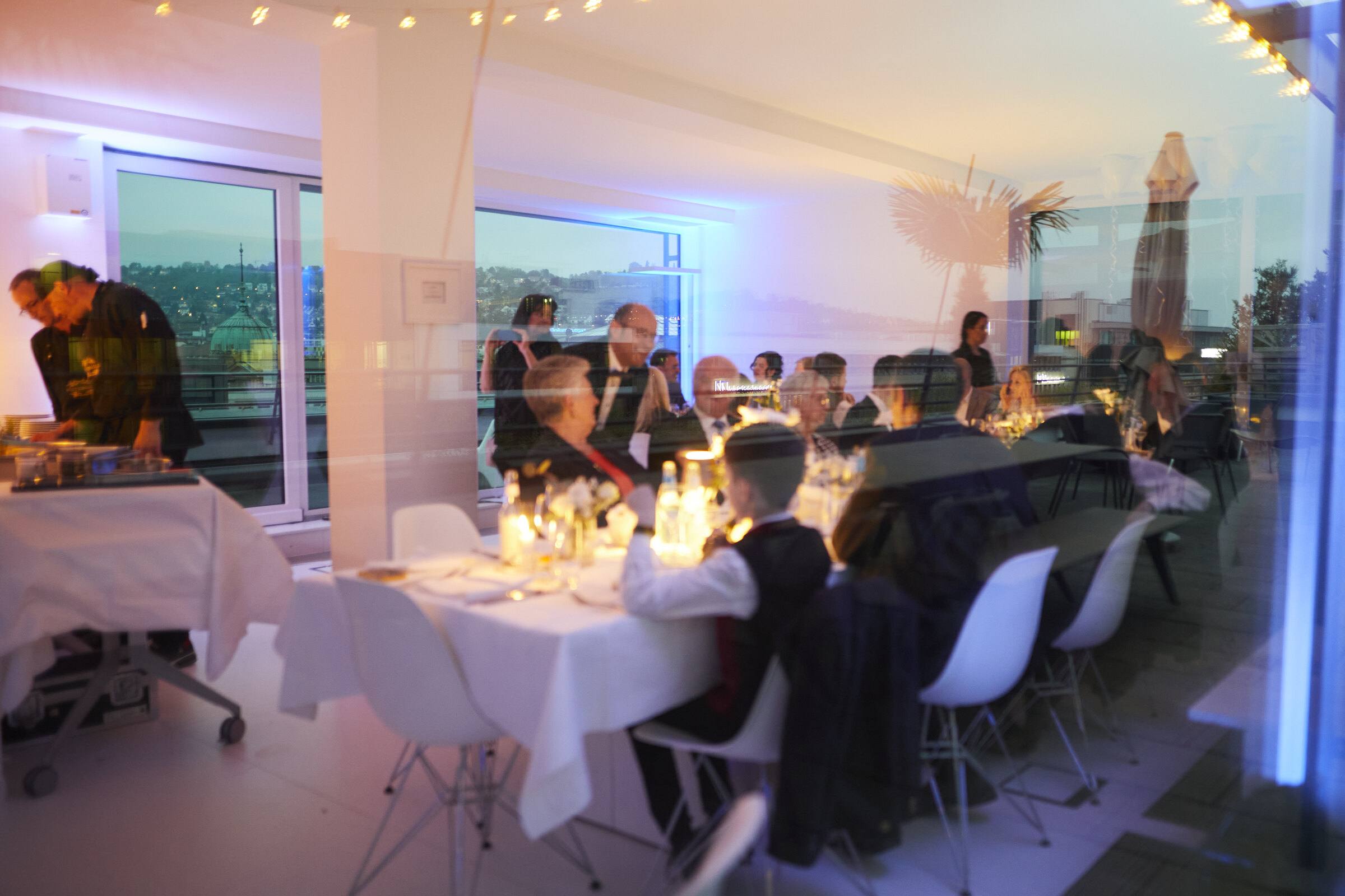 Lange Festtafel mit Kerzen in einem verglasten Dachgeschoss bei Dämmerung