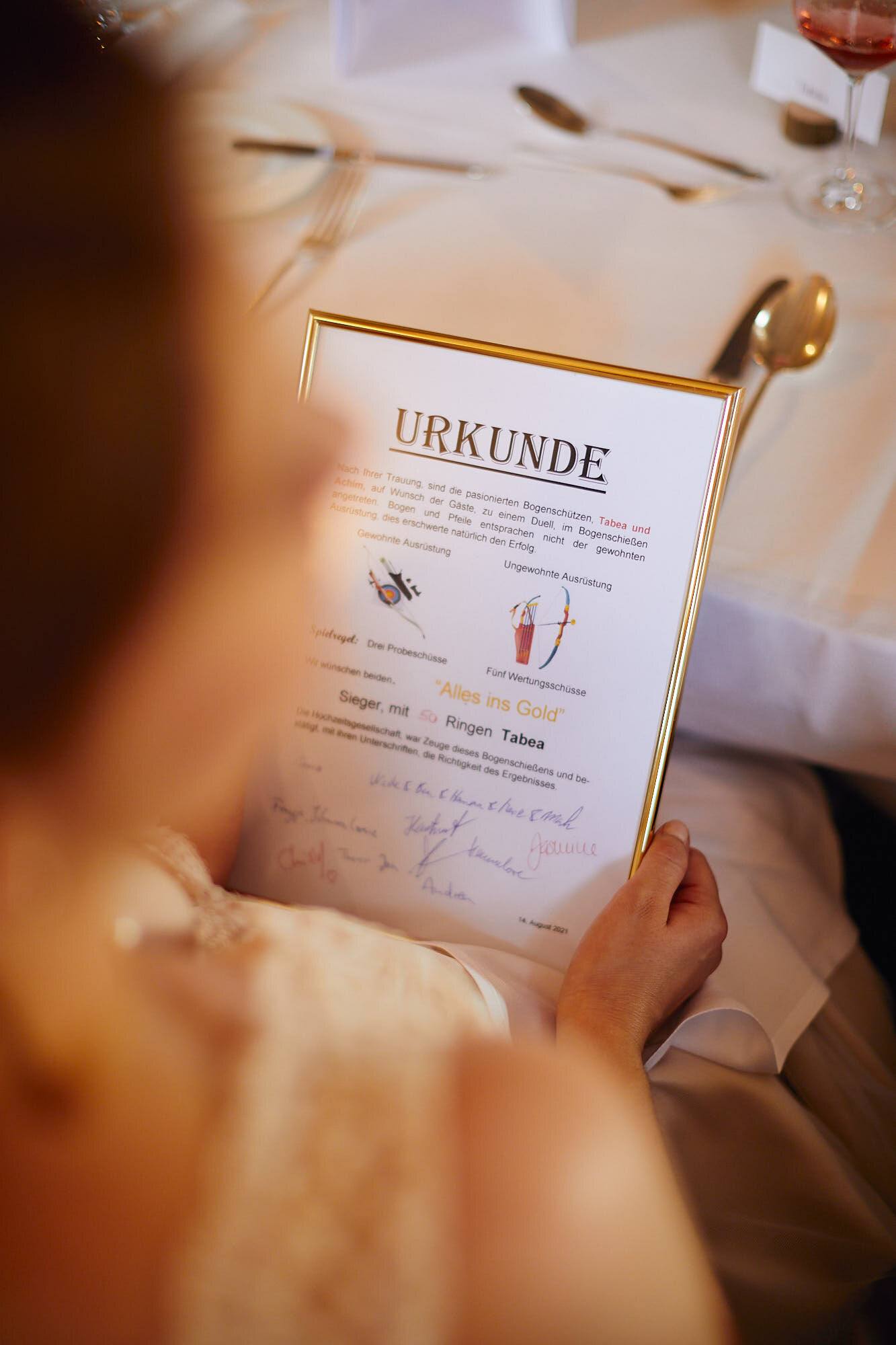 Braut liest eine gerahmte Urkunde am Tisch.