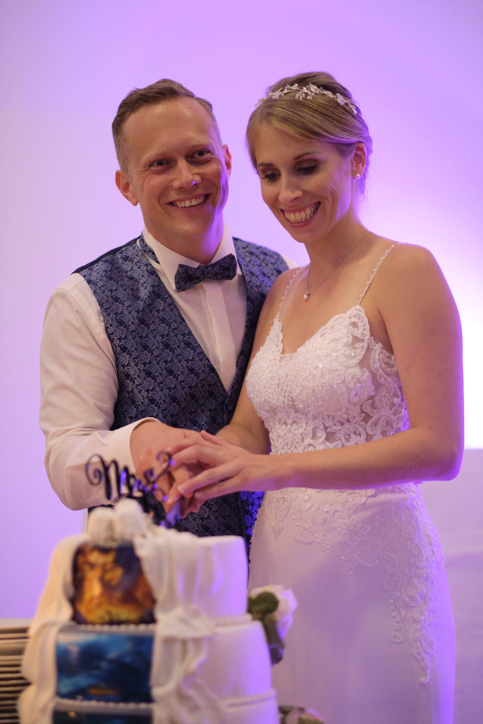 Brautpaar schneidet lachend die Hochzeitstorte im violetten Licht an