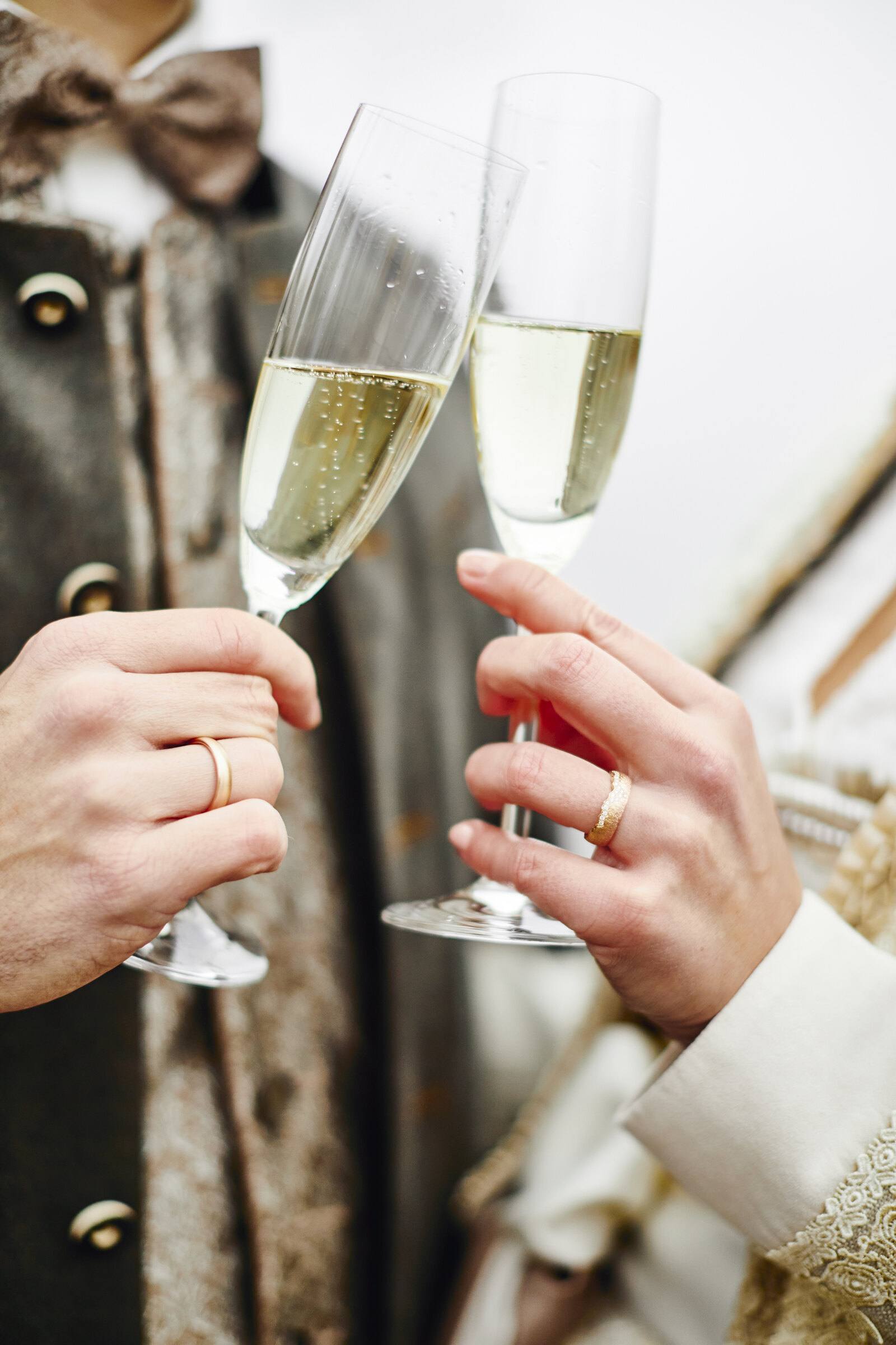 Anstoßen mit Sekt, Eheringe an den Händen und Trachtenjanker
