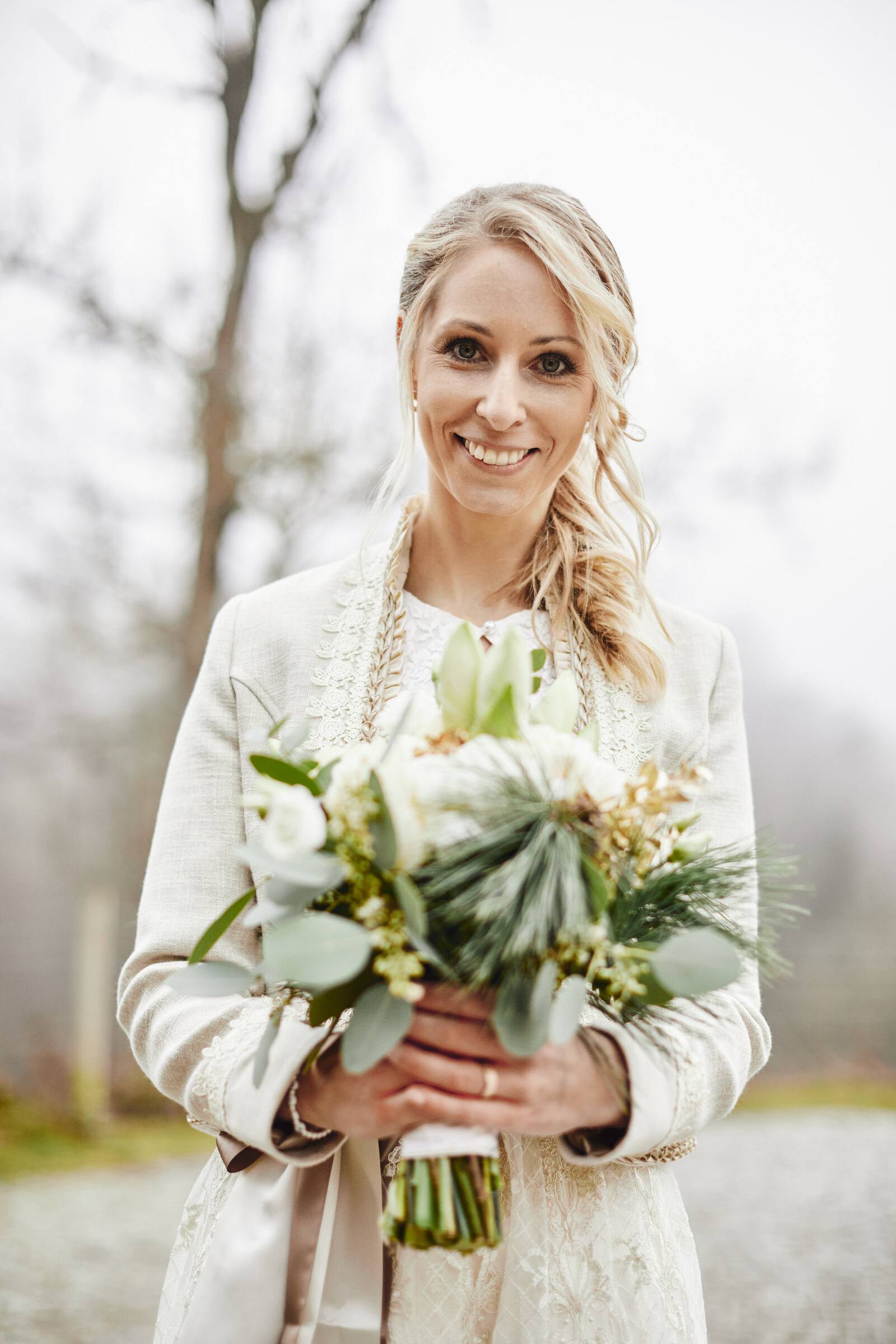 Lachende Braut im Dirndl mit Strauß vor nebligen Winterbäumen