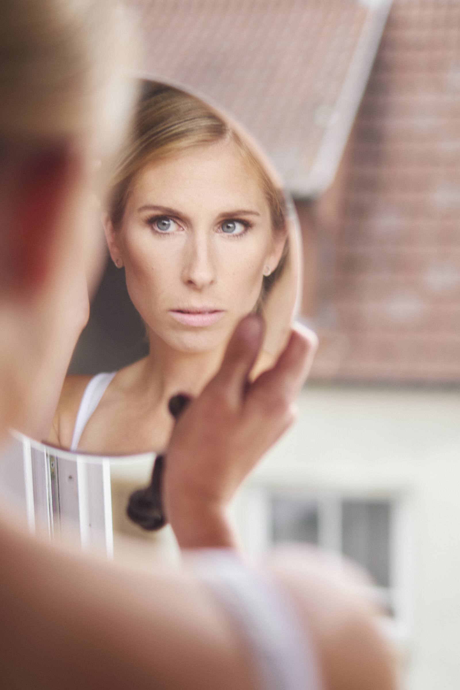 Braut betrachtet sich vor der Trauung in einem kleinen Handspiegel