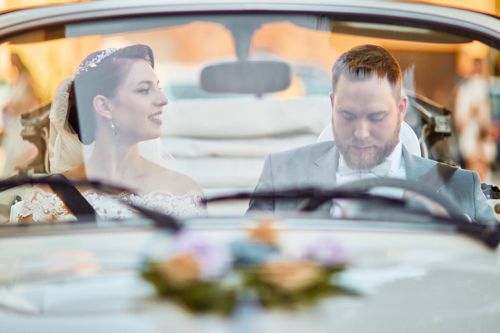 Brautpaar im offenen Hochzeitsauto, durch die Windschutzscheibe fotografiert