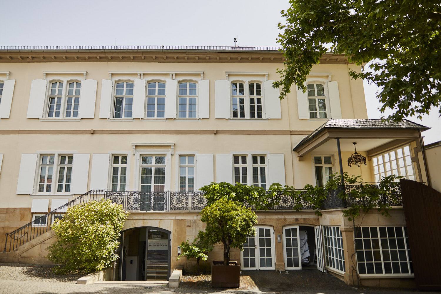 Gelbes Herrenhaus des Weinguts mit Terrasse und weißen Fensterläden im Sommer