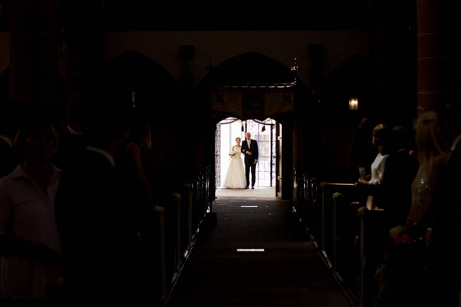 Braut und Vater erscheinen im Türlicht am Eingang der dunklen Kirche