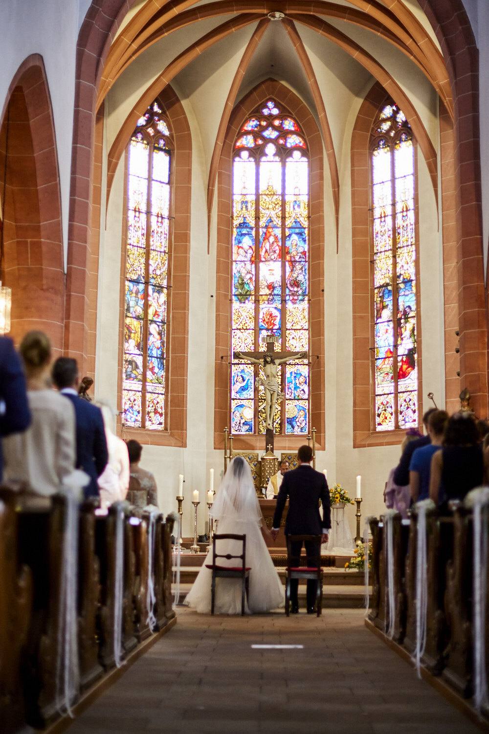 Brautpaar vor dem Altar unter drei hohen bunten Kirchenfenstern
