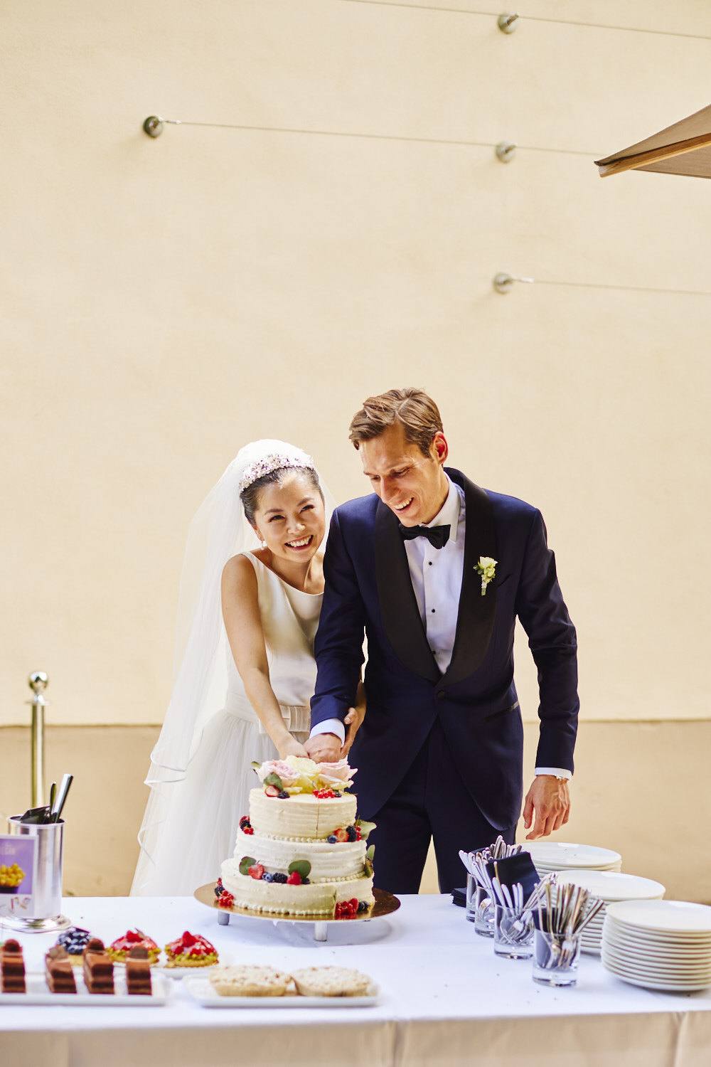 Brautpaar schneidet lachend die dreistöckige Hochzeitstorte an
