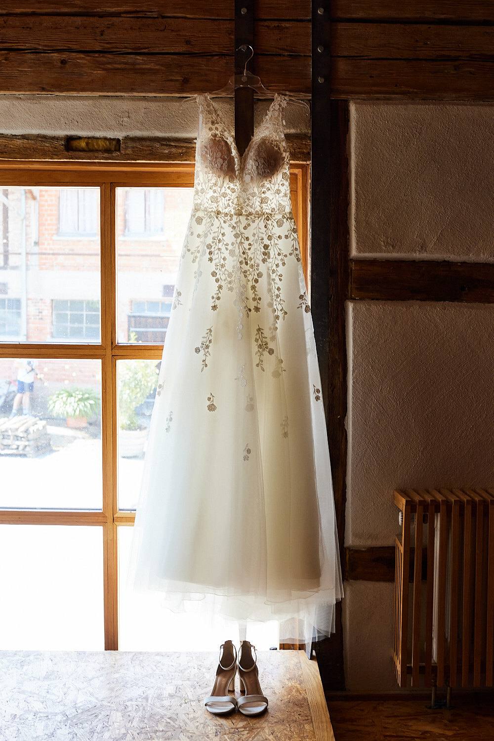 Brautkleid hängt am Fenster, Schuhe darunter.