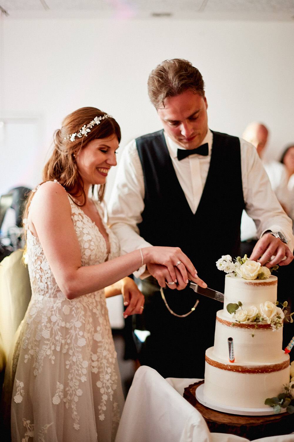 Brautpaar schneidet lachend die dreistöckige Hochzeitstorte an